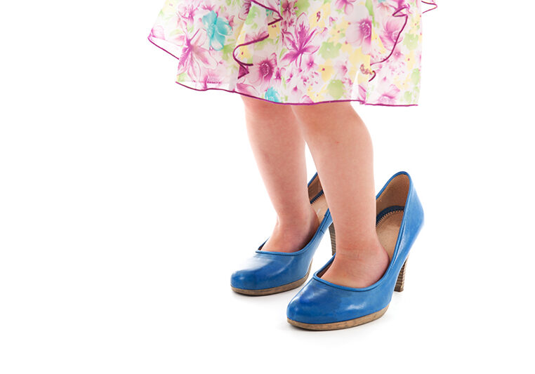 Toddler girl standing in mothers big shoes isolated over white background